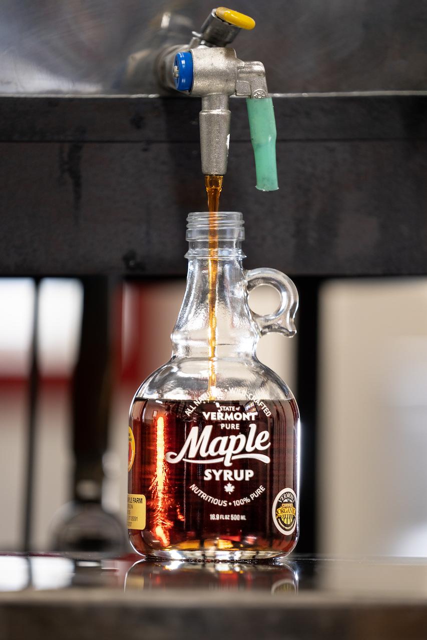Maple syrup flowing into a glass bottle from a metal tap.