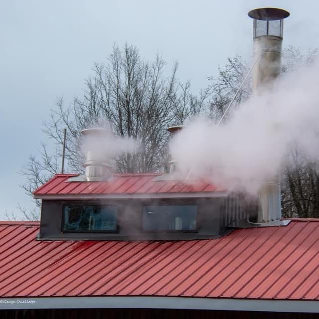 Red-roofed building with steam rising from chimneys, trees in the background.