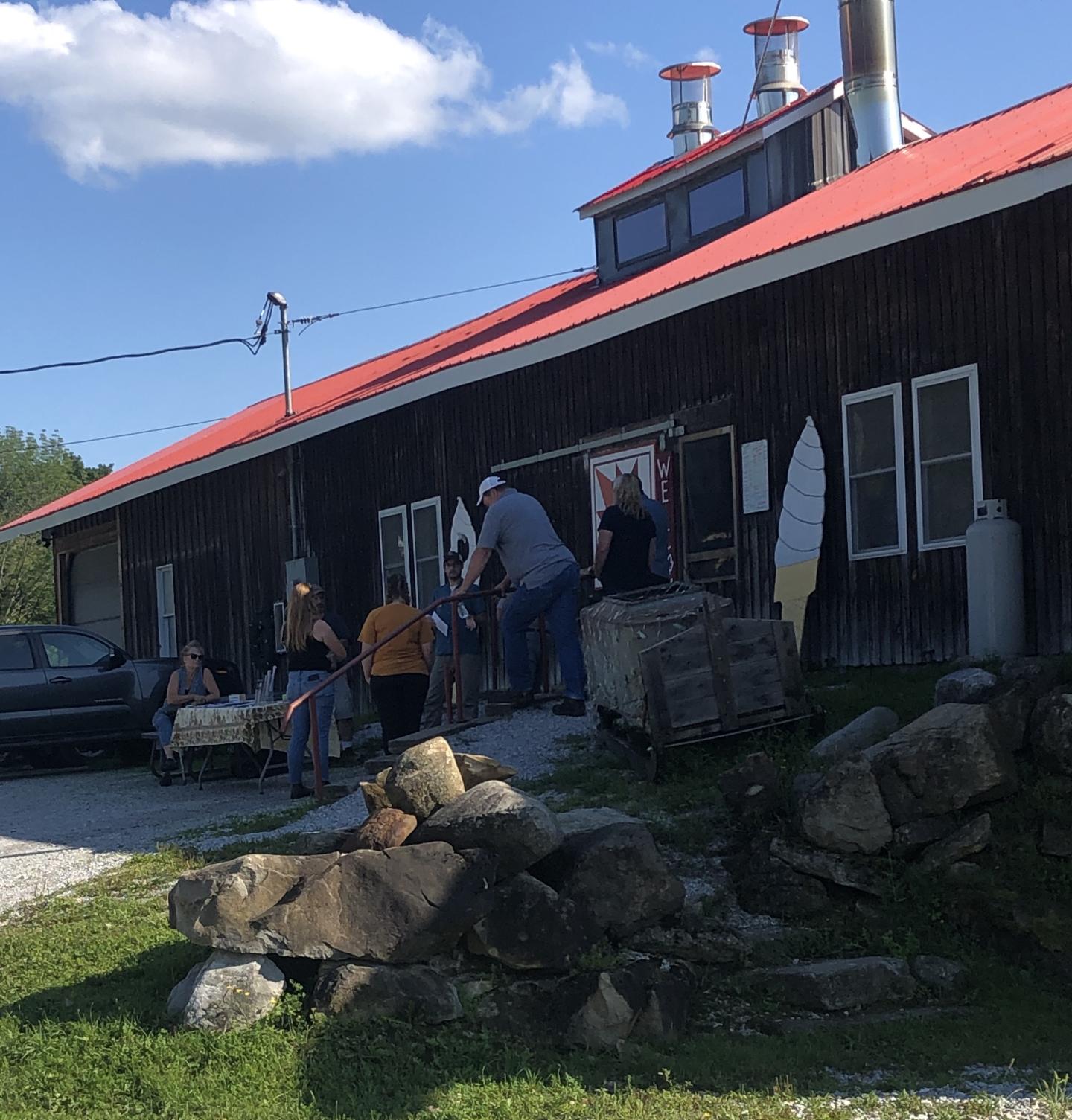 Rustic building with a red roof, people gathered outside on a sunny day.