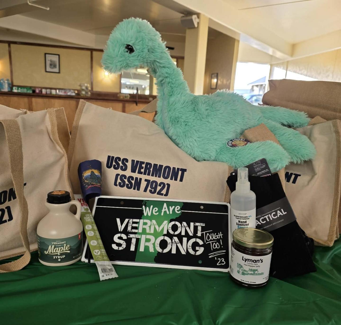 Plush dinosaur with Vermont-themed items and bags on a table.