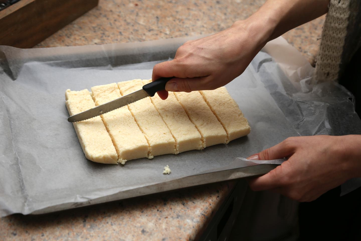 Cutting shortbread dough into strips on parchment paper.