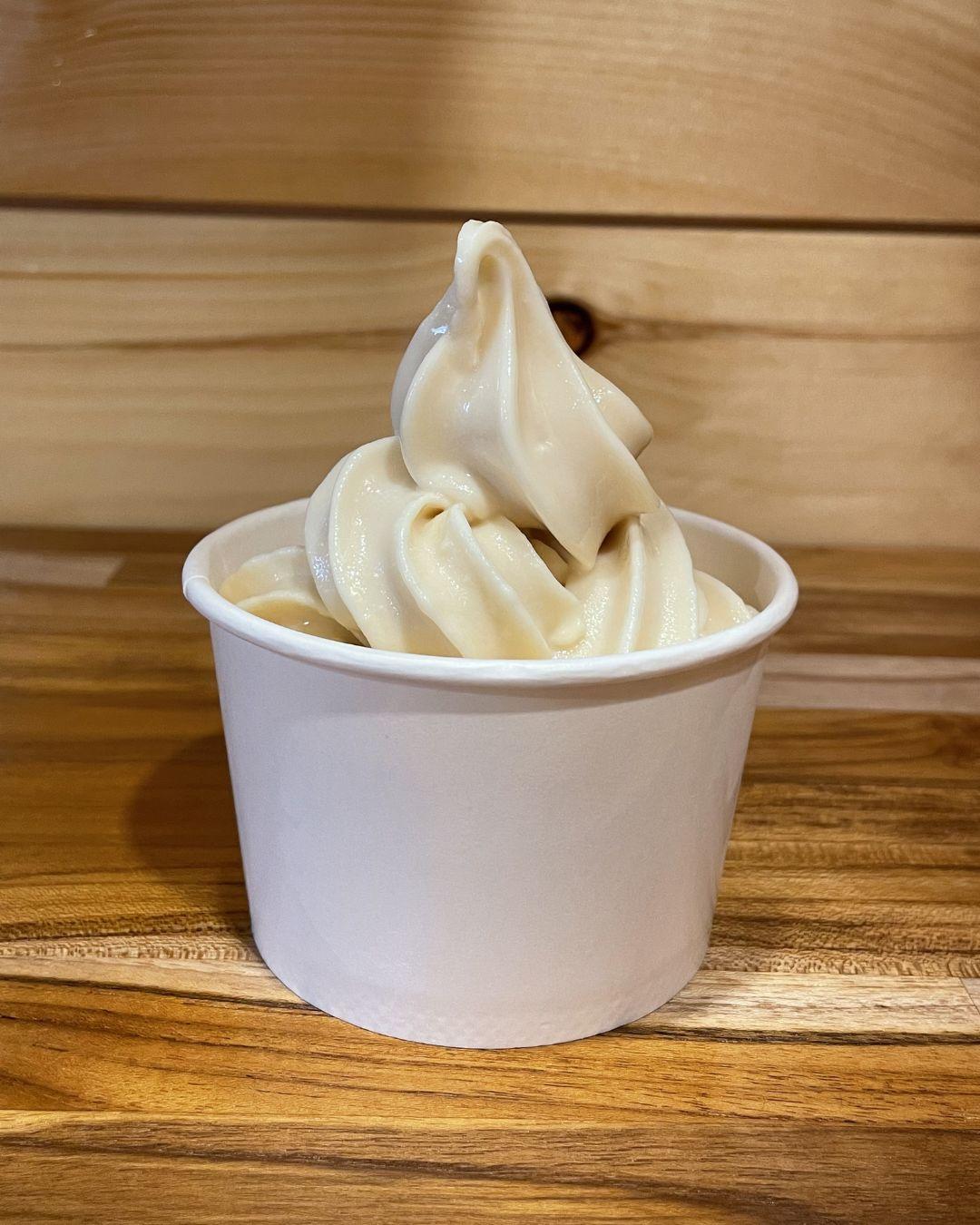 Creamy vanilla soft serve in a white cup on a wooden table.