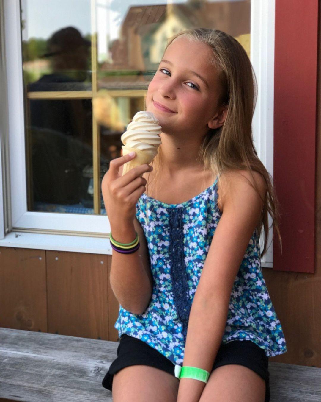 Young girl holding a vanilla ice cream cone, smiling, seated on a bench.