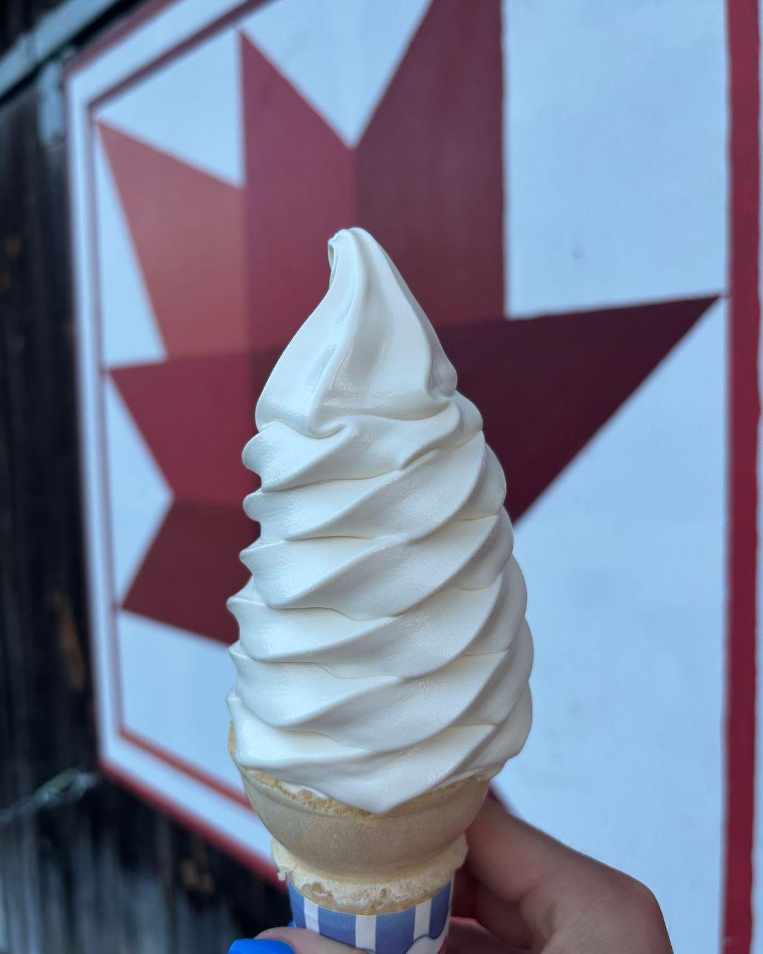 Soft serve ice cream cone held in front of a red and white geometric mural.