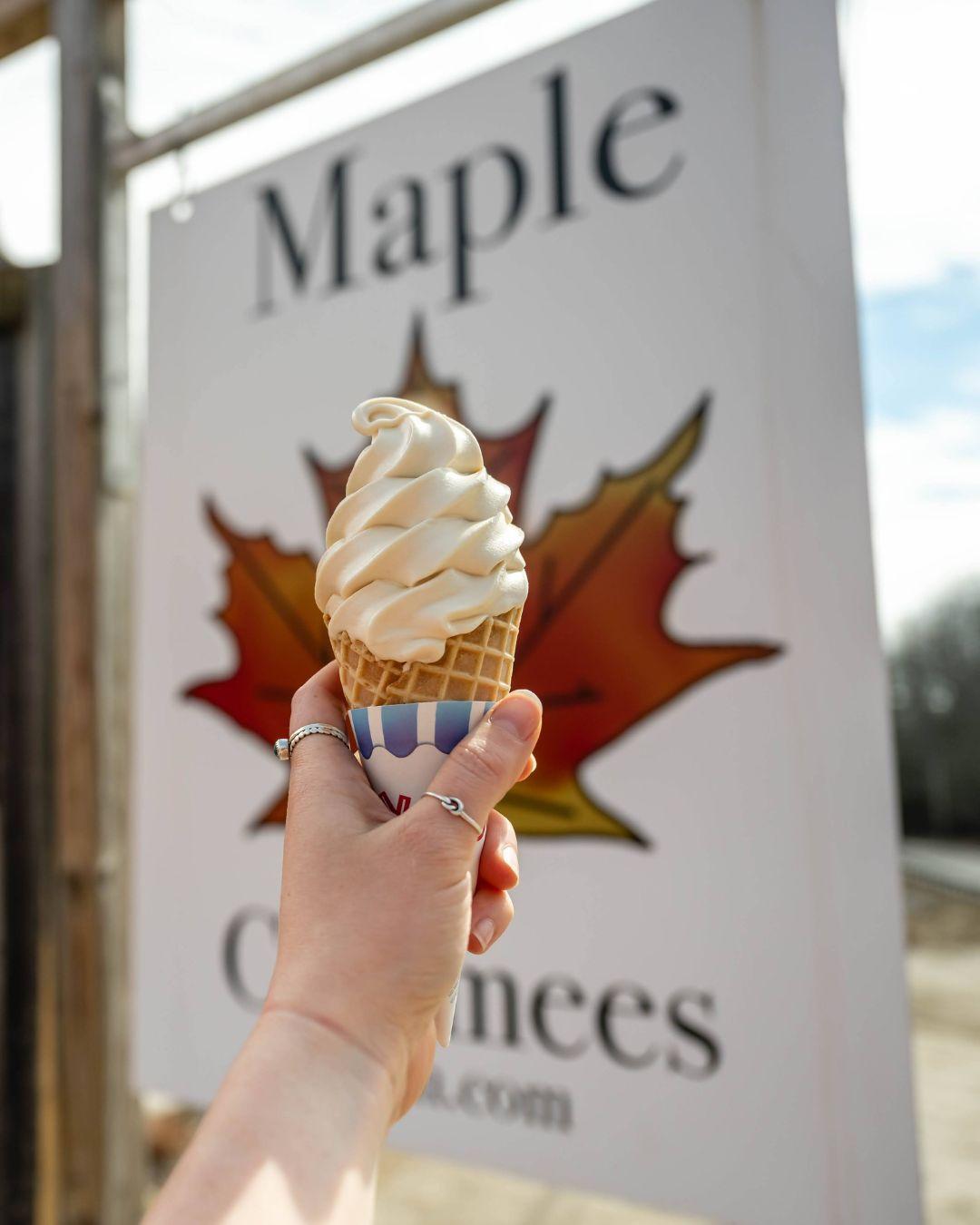 A hand holds a soft-serve ice cream cone against a maple leaf sign.