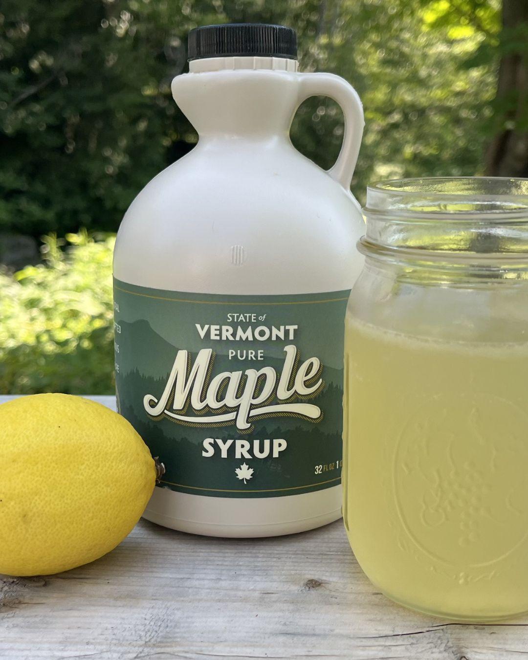 Maple syrup jug, lemon, and jar of lemonade on table outdoors.