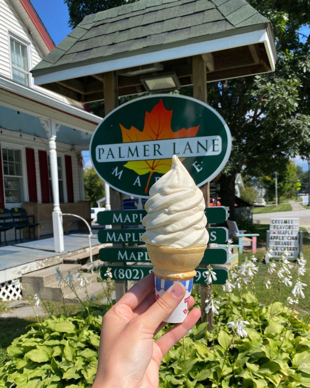 Soft serve ice cream held up in front of a "Palmer Lane Maple" sign.