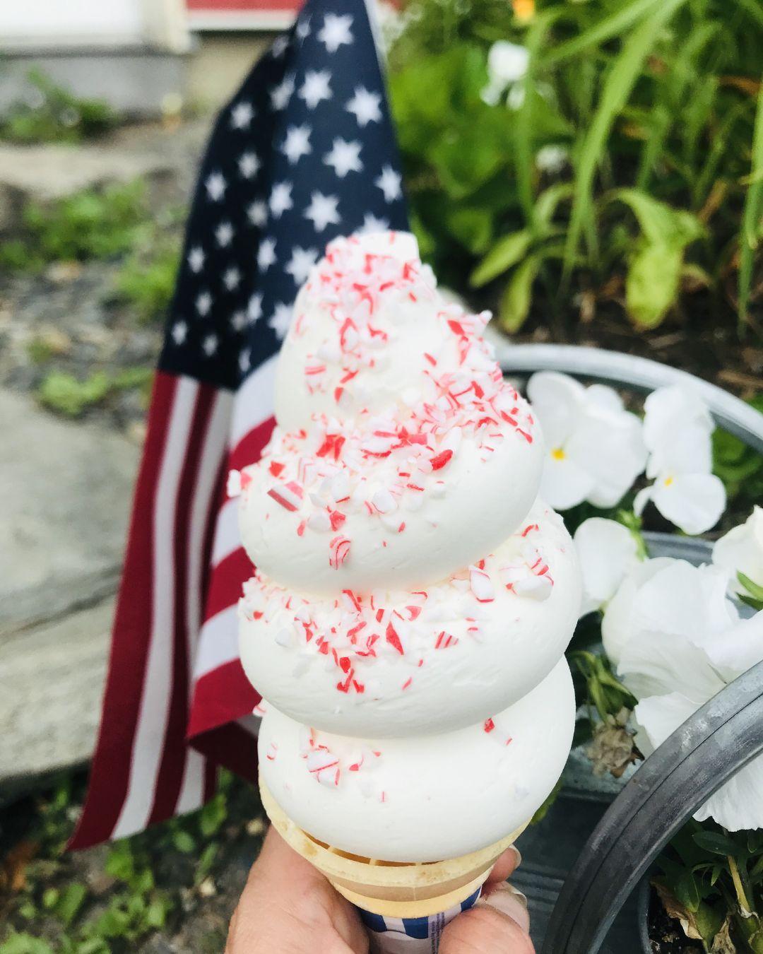 Soft serve ice cream with sprinkles, American flag in background.