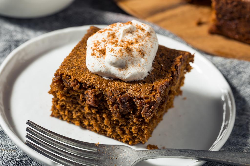 Gingerbread cake slice with whipped cream on a white plate.
