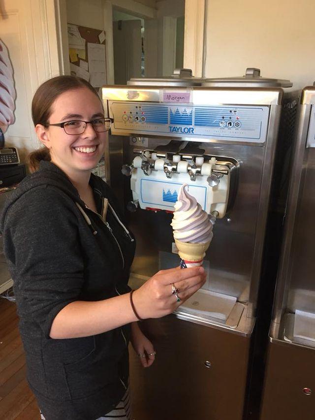 Woman smiling, holding a swirl ice cream cone by ice cream machine.