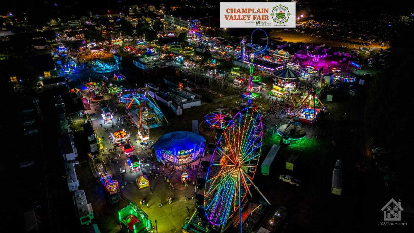Colorful nighttime aerial view of a fairground with rides and bright lights.