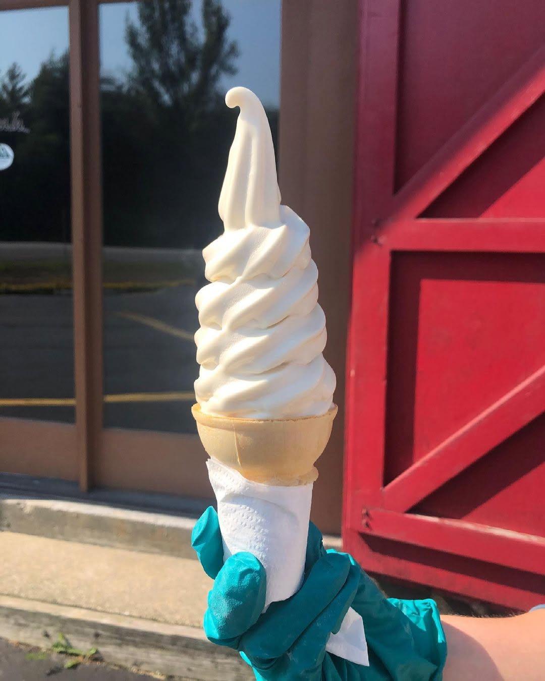 Soft-serve ice cream cone held by a gloved hand in sunlight.