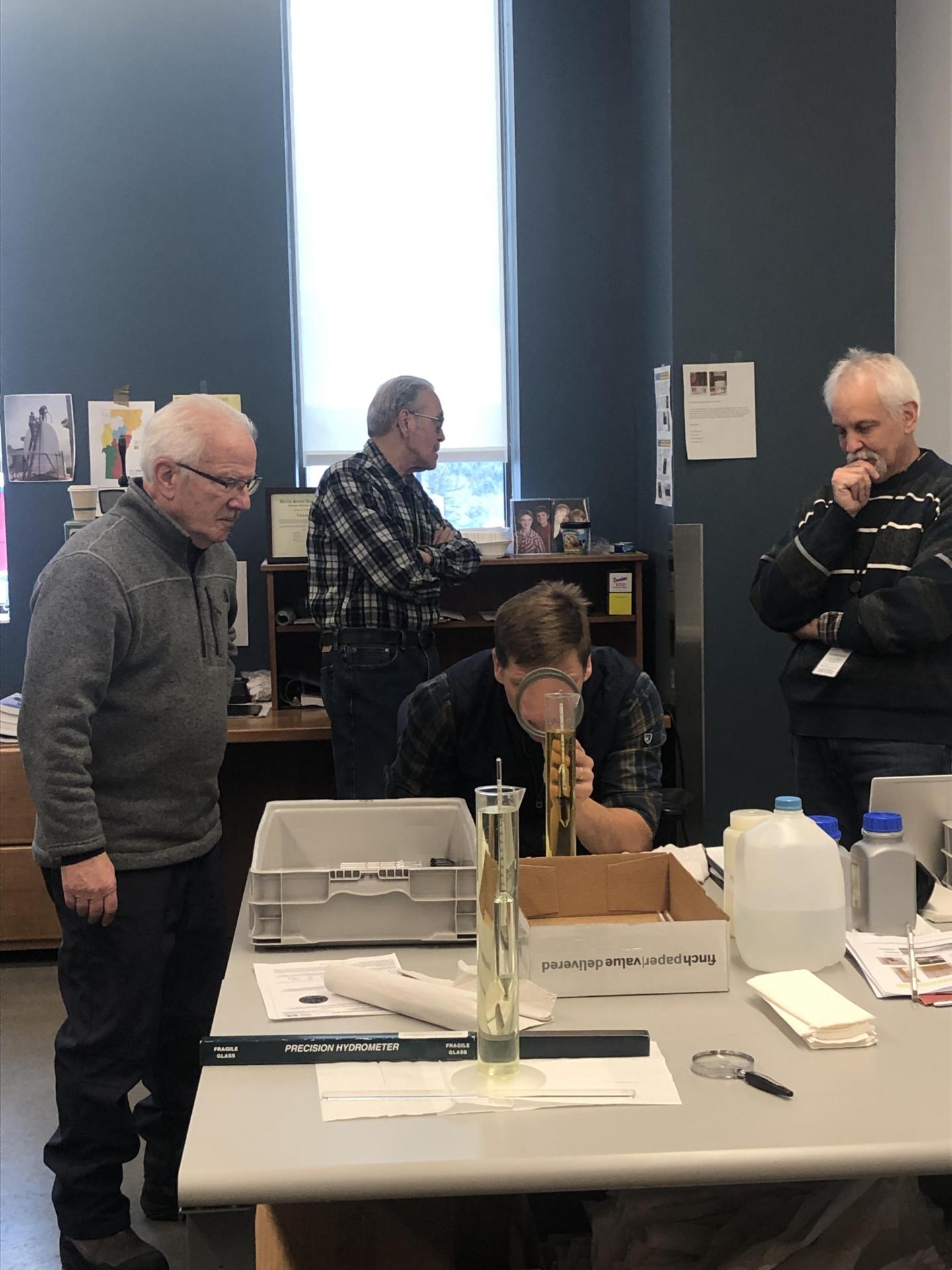People examining a tall glass instrument in a room.