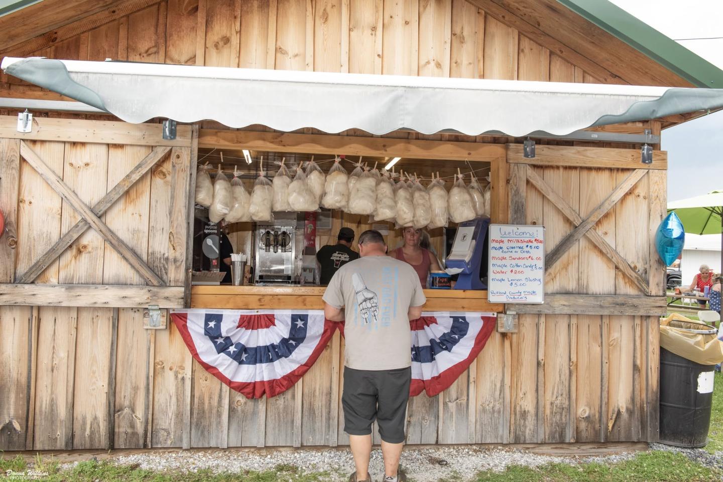 Man standing at a wooden food stall with American flags.