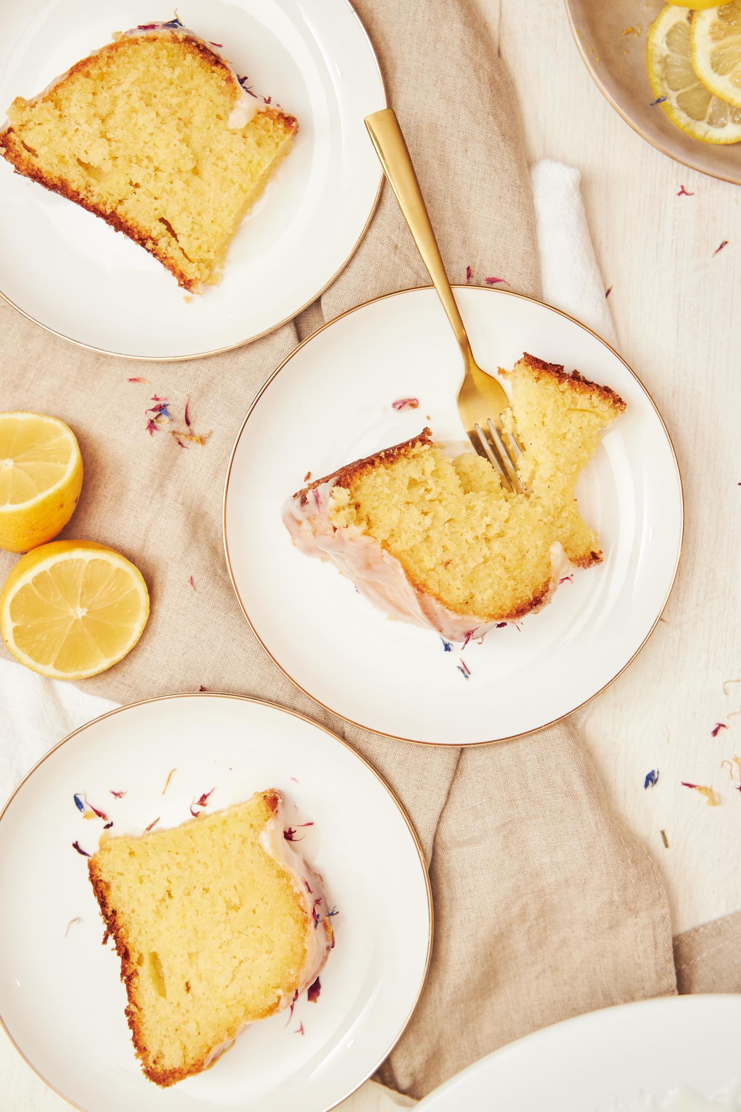 Lemon cake slices on white plates with a fork, surrounded by lemon halves.