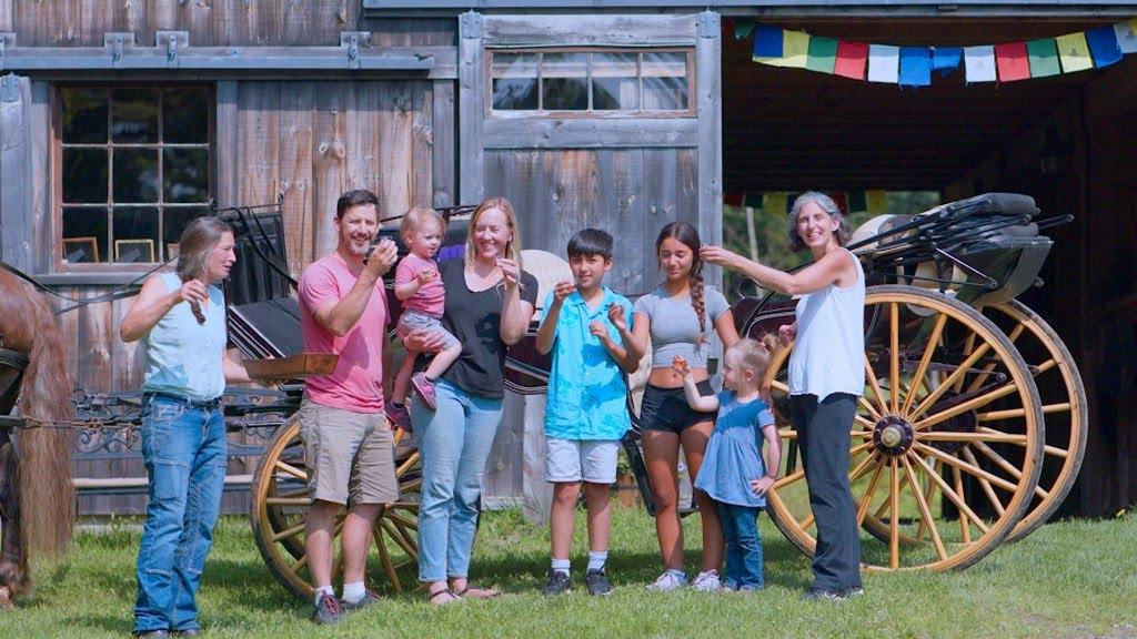 Group of people smiling in front of a rustic wooden building with a wagon.